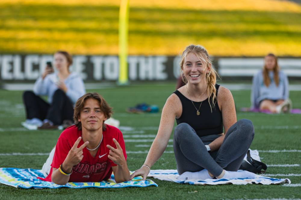 Two students stretching and sitting on the Football Field during a yoga session at sunset